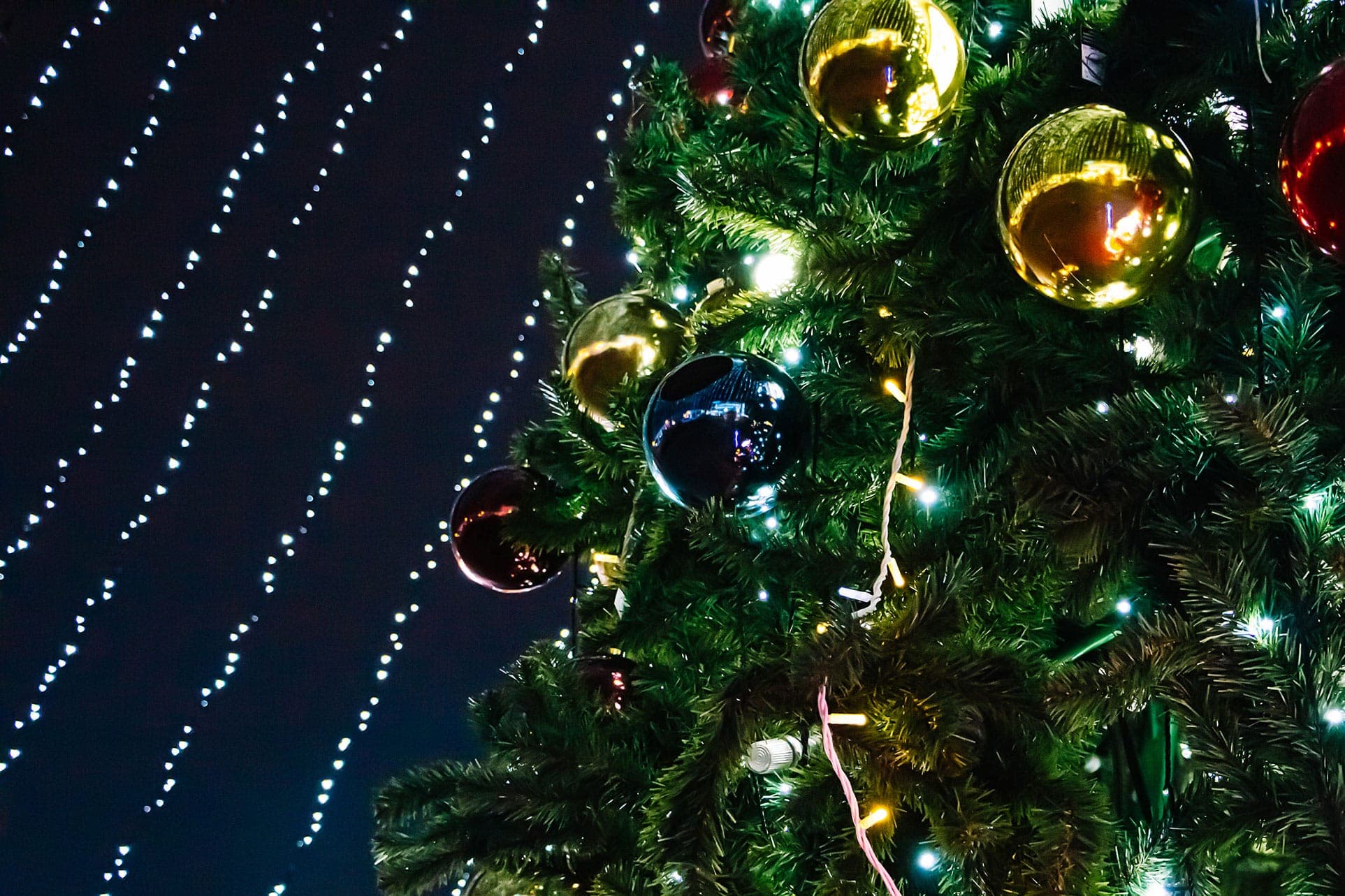 A lit holiday tree glowing in a snowy mountain town at night